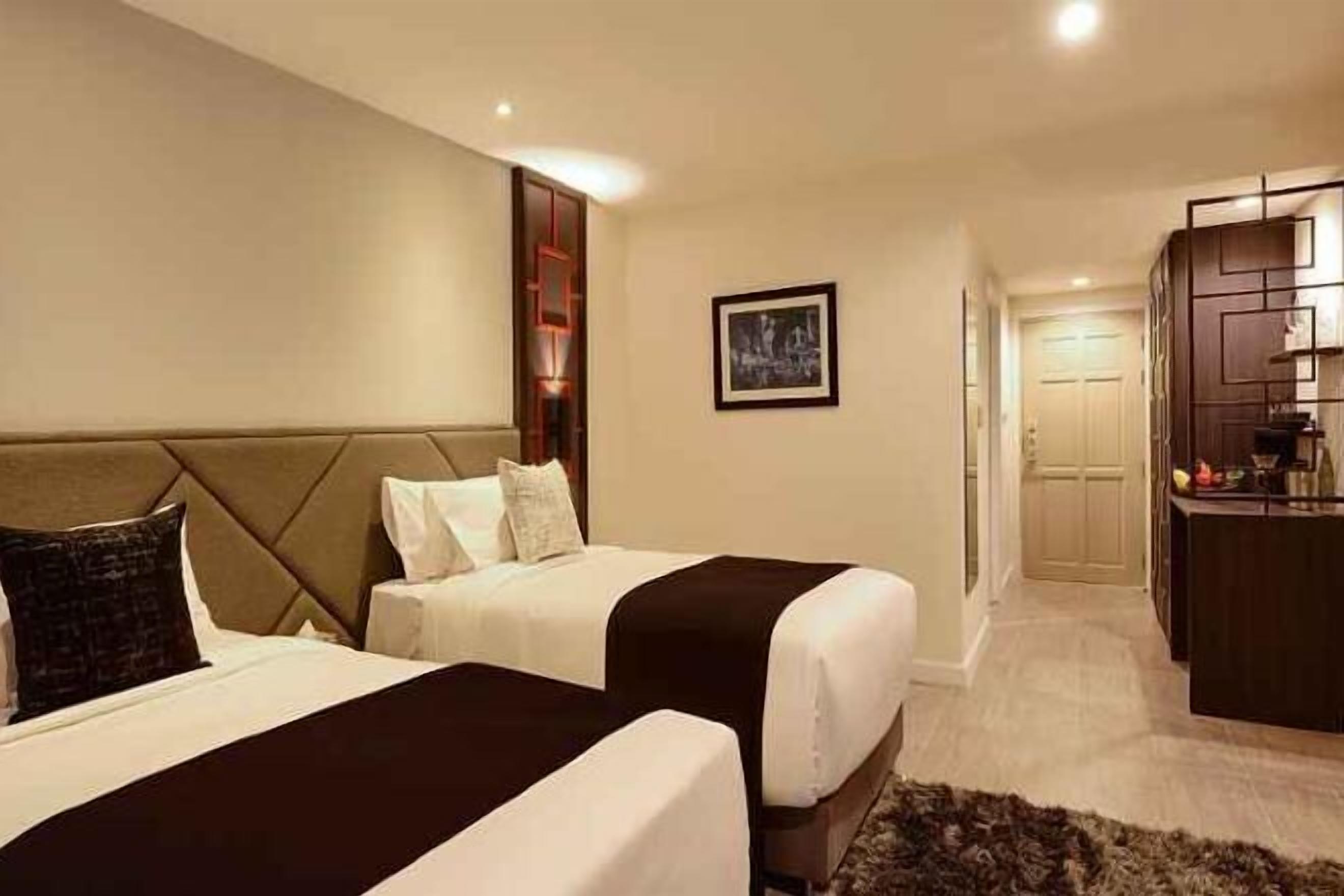 Een hotelkamer met twee bedden, een kleine kitchenette en een deur naar een gang.
