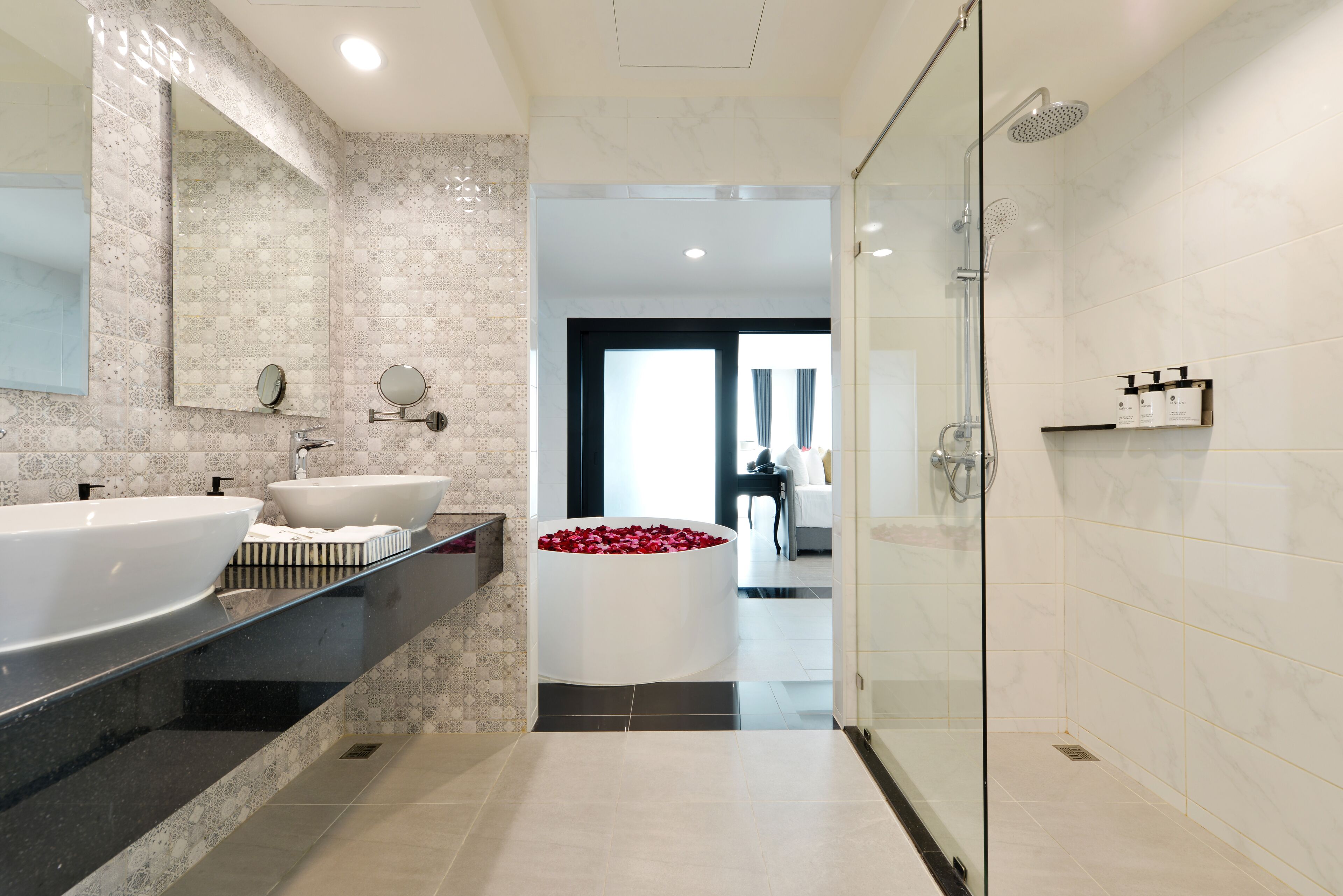 A modern bathroom with two sinks, a large bathtub with red flowers, and a glass shower enclosure.