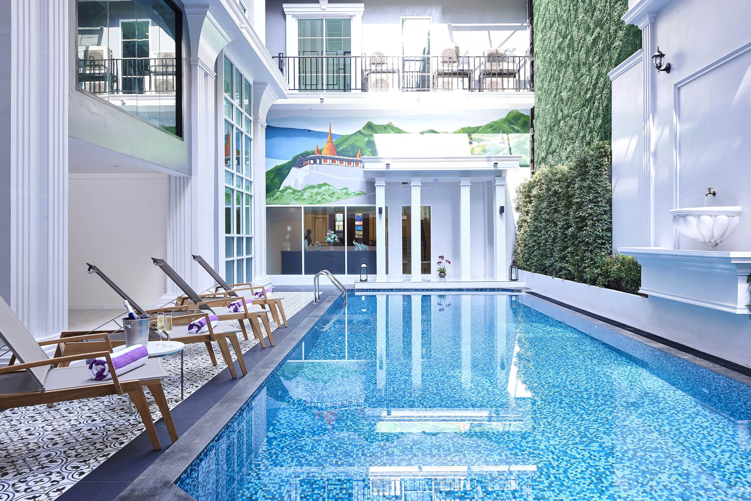 A pool area with lounge chairs, a clear pool, and a mural of a mountain landscape.