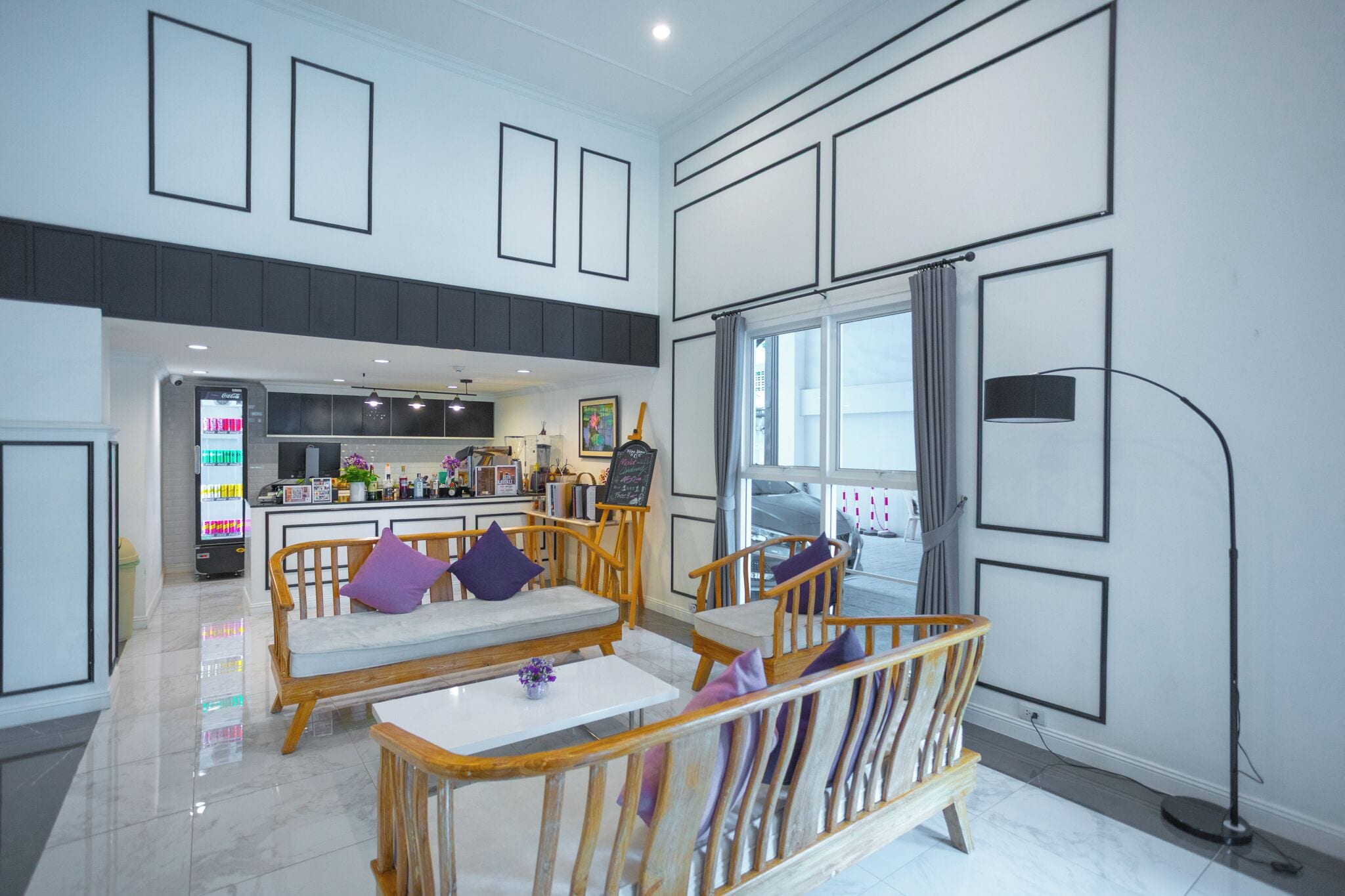 A spacious living area with a kitchen in the background, wooden furniture, and large windows.