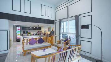 A spacious living area with a kitchen in the background, wooden furniture, and large windows.