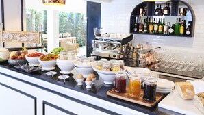 Un bufé de desayuno con diferentes opciones de comida, una zona de bar con botellas y vasos, y vistas a zonas verdes al exterior.