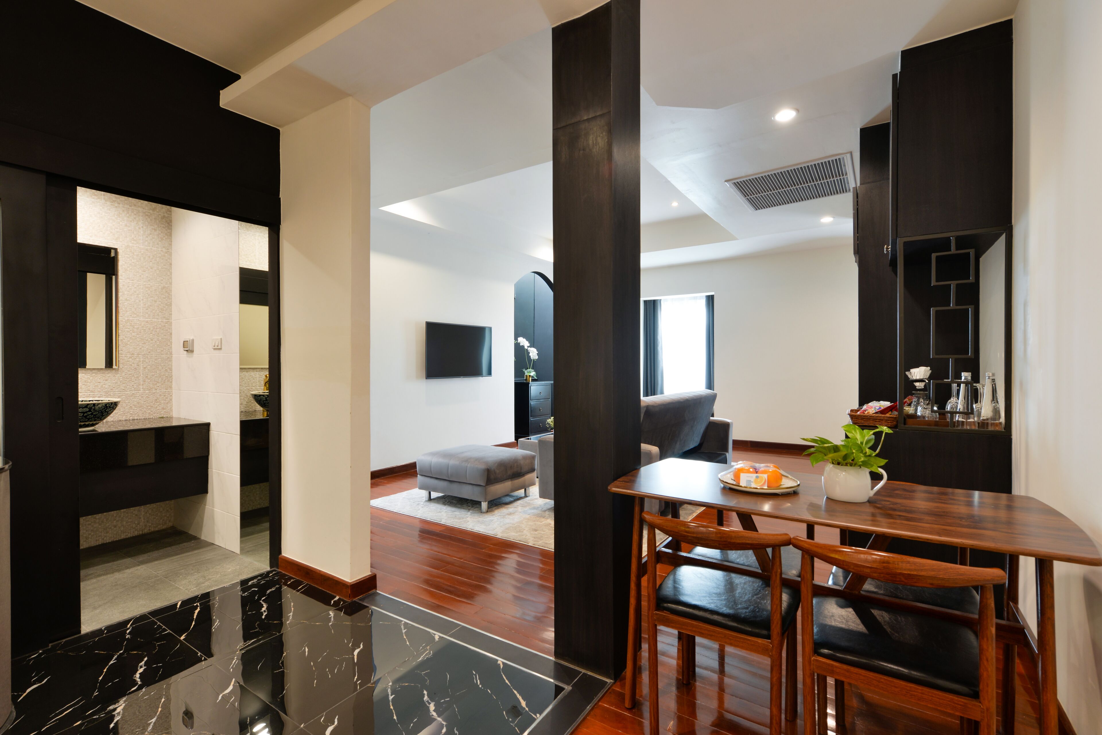 A modern living room with a dining area, featuring a marble floor, dark wooden furniture, and a large window providing natural light.