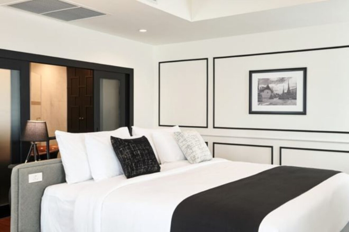 Una habitación de hotel moderna con una cama grande, un escritorio y una silla. Hay un cuadro en la pared y una lámpara sobre el escritorio.