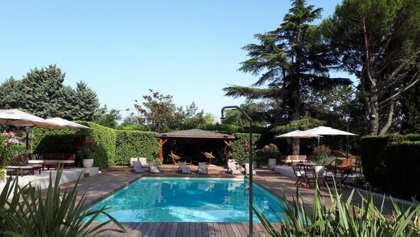Piscina rectangular con cubierta de madera, rodeada de sillas de descanso y sombrillas.