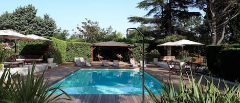 Piscina rectangular con cubierta de madera, rodeada de sillas de descanso y sombrillas.