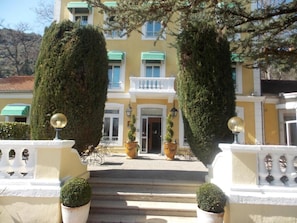 A building with a yellow facade, white balconies, and a central entrance with steps. - Logis Hotel le Cedre de Soyons (Soyons)