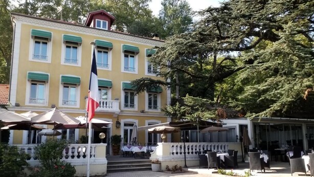 A two-story building with a balcony, outdoor seating area, and a flag. - Logis Hotel le Cedre de Soyons (Soyons)