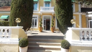 A building with a yellow facade, white balconies, and a central entrance with steps. - Logis Hotel le Cedre de Soyons (Soyons)