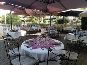 An outdoor dining area with round tables set for a meal, surrounded by umbrellas and metal chairs. - Logis Hotel le Cedre de Soyons (Soyons)