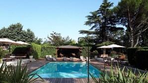 A rectangular swimming pool with a wooden deck surrounding it, lounge chairs, and umbrellas. - Logis Hotel le Cedre de Soyons (Soyons)