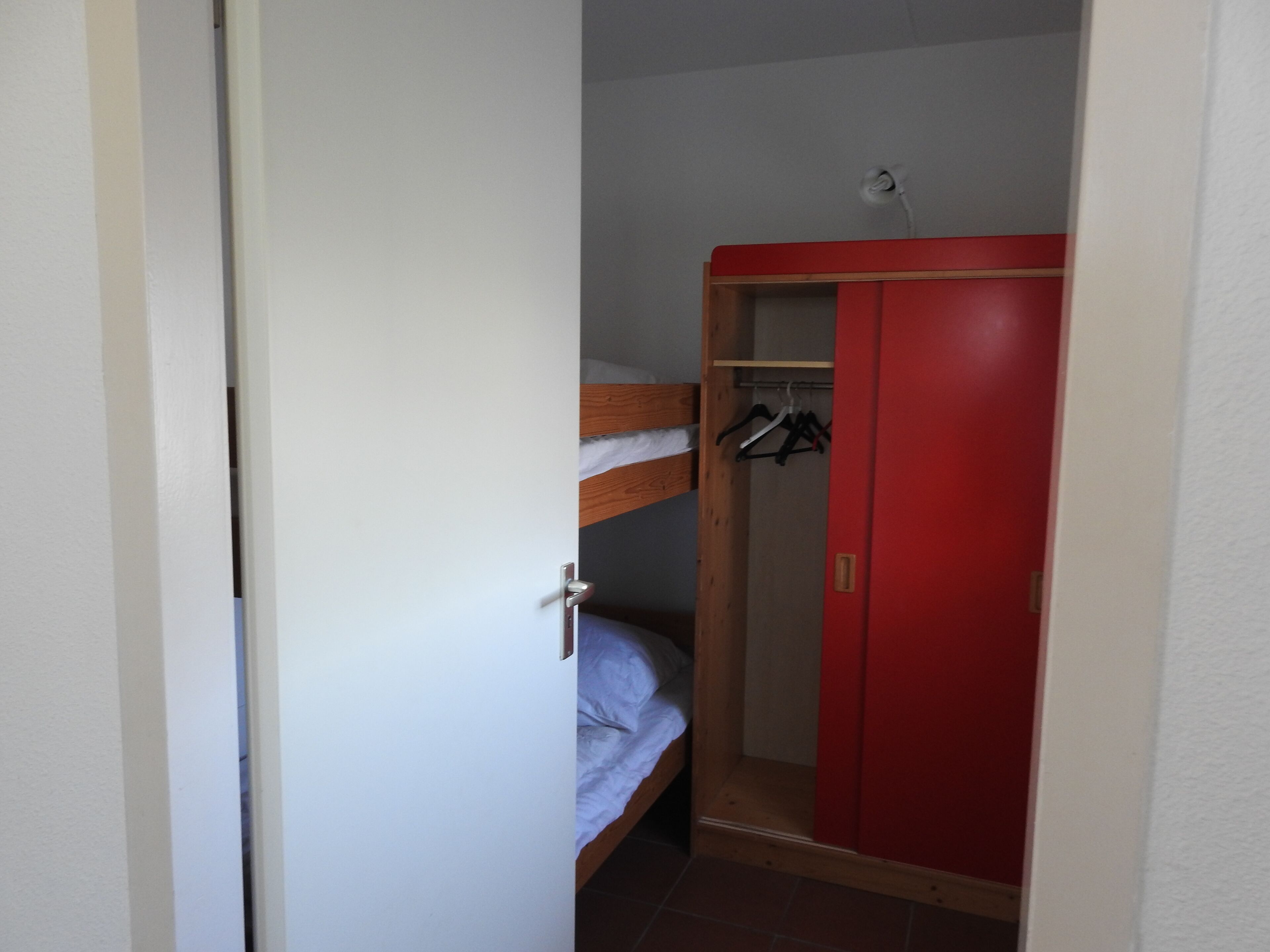 A small room with a bunk bed, a red wardrobe, and a door.