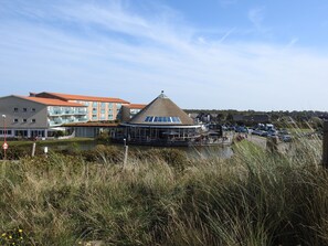 Un bâtiment situé au bord de l’eau, doté d’un toit de chaume et d’une extension en verre, entouré d’une pelouse et d’un parking.