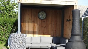 Un patio con pared de madera, un reloj, un pilar de piedra y una parrilla grande de color negro.