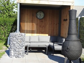 Un espace patio agrémenté d’un mur en bois, d’une horloge, d’un pilier en pierre et d’un grand barbecue noir.
