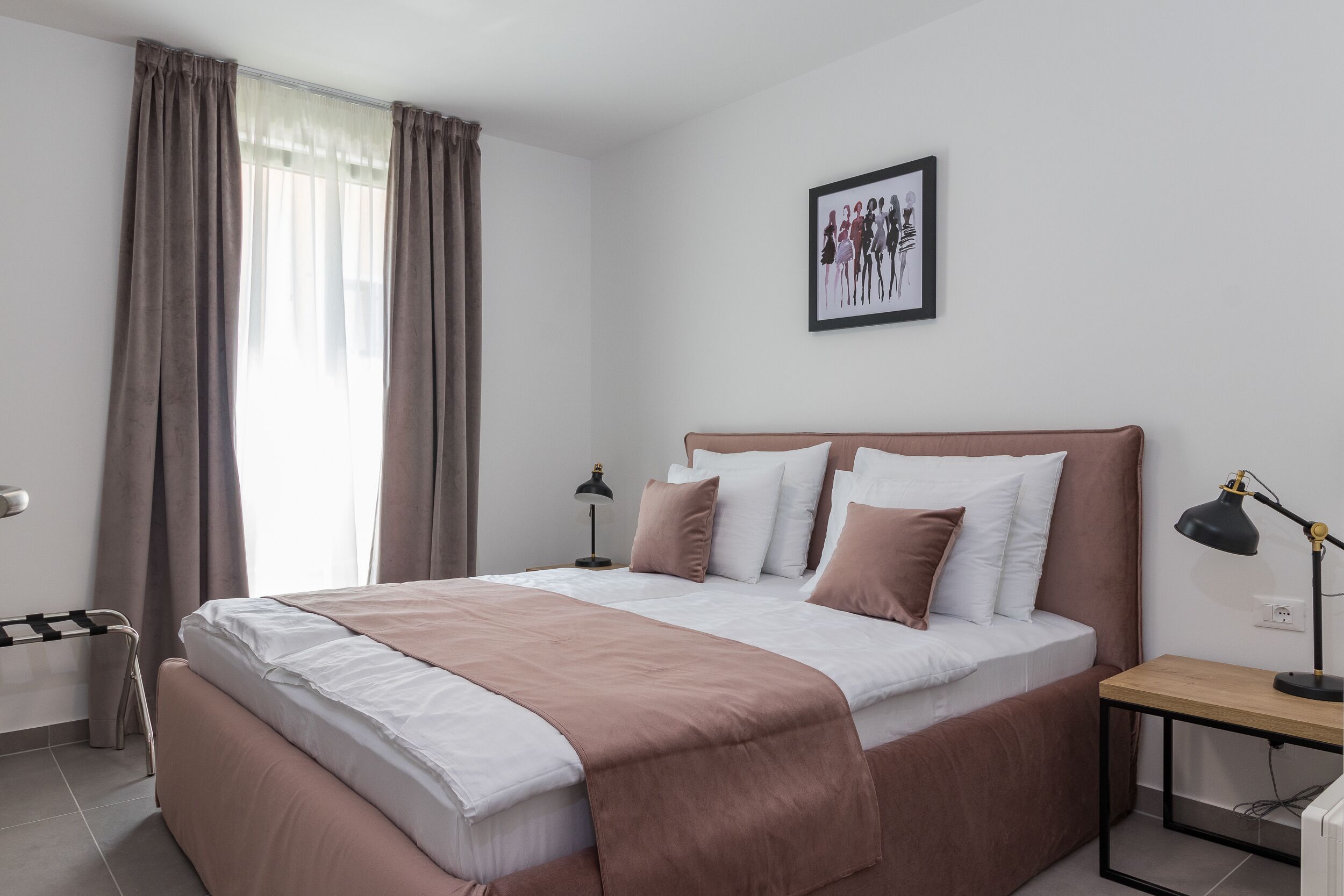 Un dormitorio ordenado con una cama grande, mesitas de noche, un cuadro en la pared y una ventana con cortinas.