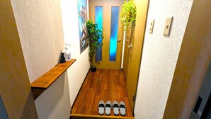 Un pasillo estrecho con suelo de madera, un estante de madera, una planta en maceta y una puerta con paneles de vidrio esmerilado.