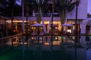Un hotel moderno con piscina, sillas de descanso y palmeras.