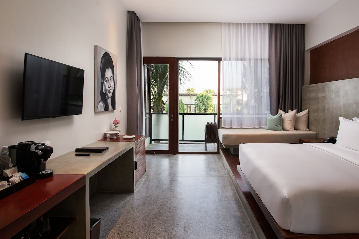 Une chambre d’hôtel équipée d’un lit, d’un bureau, d’une télévision et d’un balcon donnant sur un espace verdoyant.