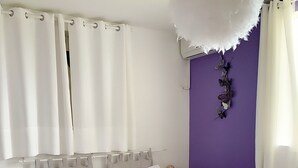 Een keurig opgemaakt bed met kussens en een handdoekdecoratie in de vorm van een zwaan, een zachte witte decoratie aan het plafond en een paarse accentmuur met vlinderdecoraties.