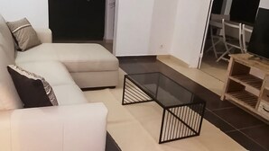 Een woonkamer met een bank, een glazen salontafel en een houten bijzettafeltje.
