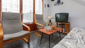 Una sala de estar con un sofá, dos sillones, una mesa baja, un televisor y una estantería.