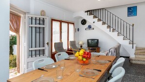 Un comedor con una mesa de madera dispuesta para cuatro personas, un televisor y una escalera.