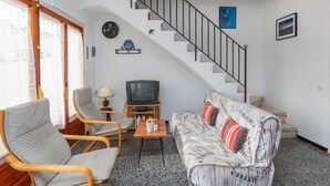 Una sala de estar con sofá, dos sillones, una mesa de centro, televisor, escalera y ventana con cortinas.