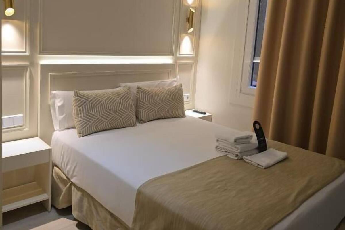 A hotel room with a large bed, bedside tables, a nightstand, a lamp, and a window with curtains.