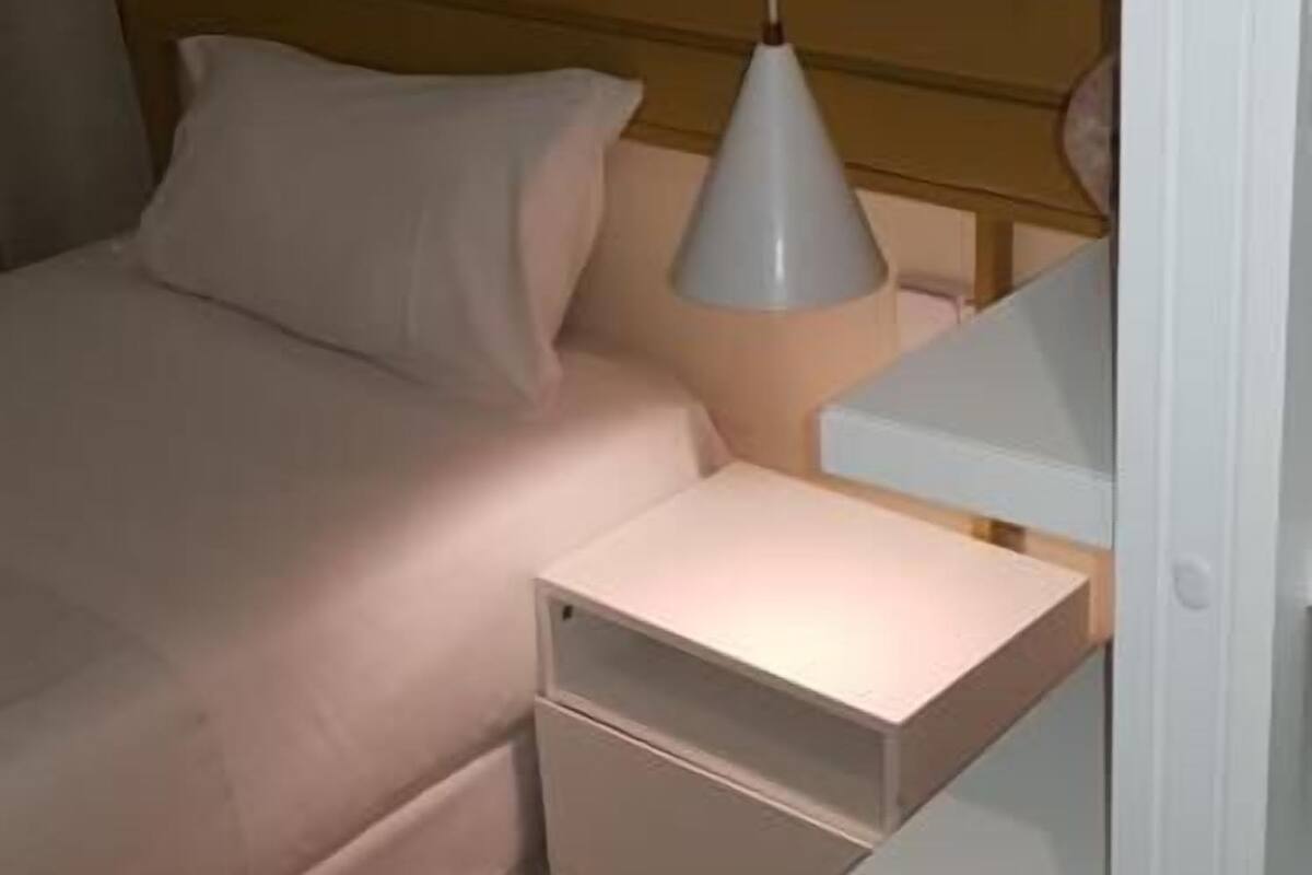 A bedroom with a bed, a bedside table, a nightstand, and a hanging light fixture.
