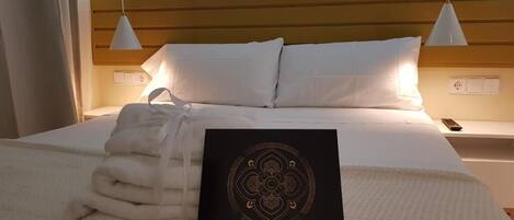 Una cama bien hecha con sábanas blancas, una toalla doblada y una tarjeta negra con 'LE PETIT PALU' escrito en ella.