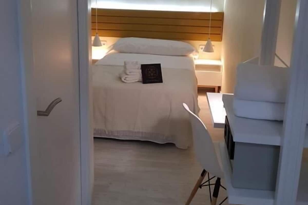 A hotel room with a bed, bedside table, and a chair.