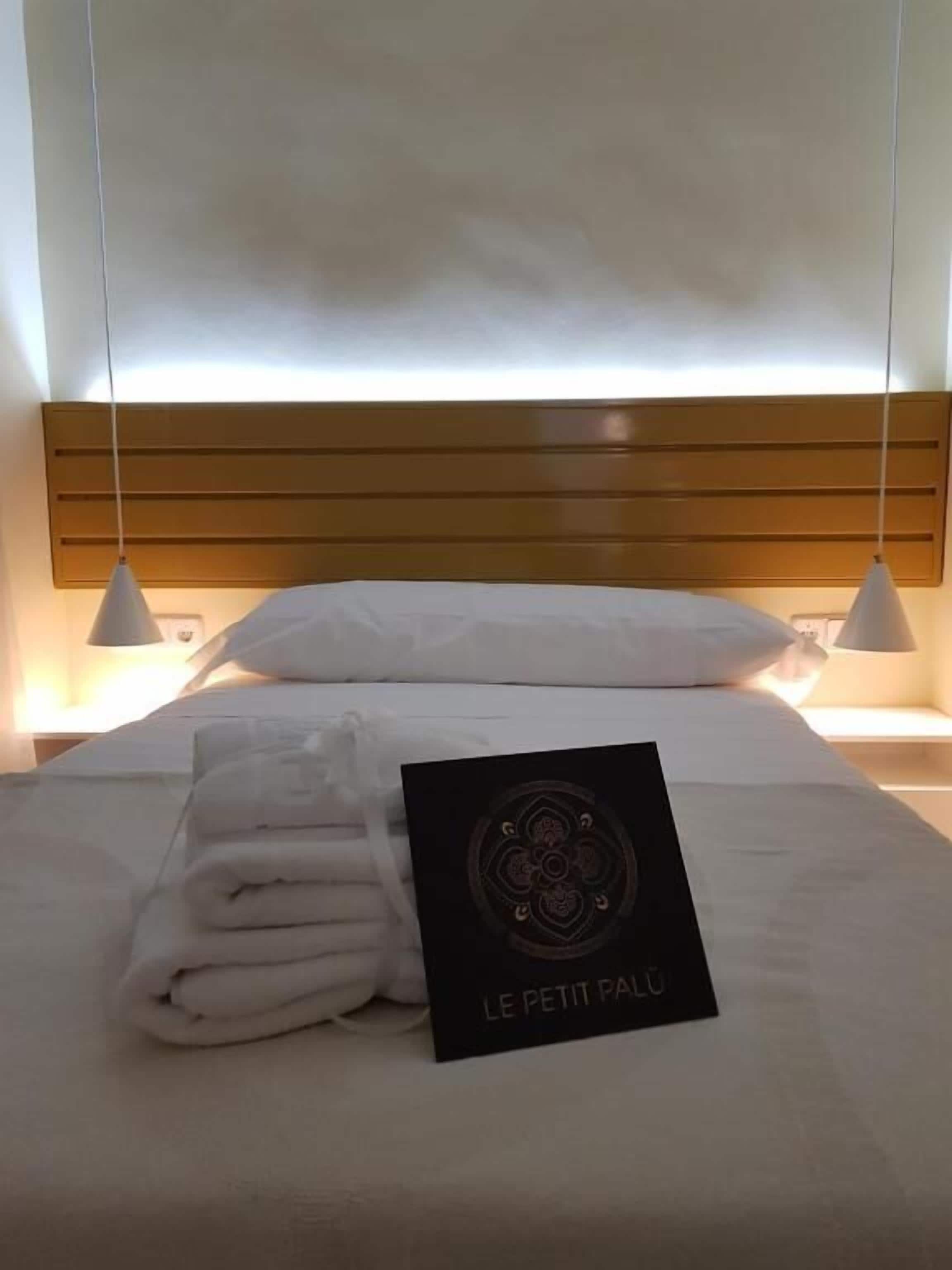 Una cama bien hecha con toallas dobladas y una tarjeta que dice "LE PETIT PAU" en una habitación de hotel.