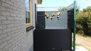 A corner of a building with a brick wall, a window, and a black outdoor seating area with a metal fence and plants. - Cozy vacation home in Julianadorp Strandslag (Julianadorp)