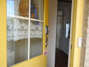 Une porte jaune avec un vitrage dépoli, un paillasson, une sonnette et un panneau « interdiction de fumer ».