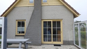 A two-story house with a stone facade, a pitched roof, and a large sliding glass door. - Cozy vacation home in Julianadorp Strandslag (Julianadorp)