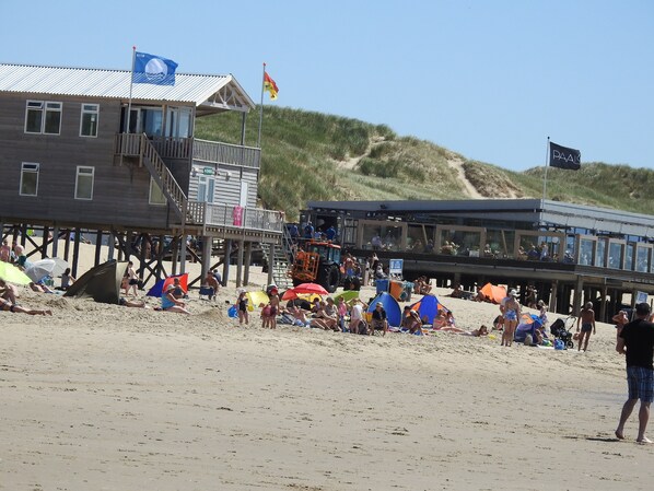 Un bâtiment situé au bord de la plage, doté d’une terrasse en bois et d’un drapeau.