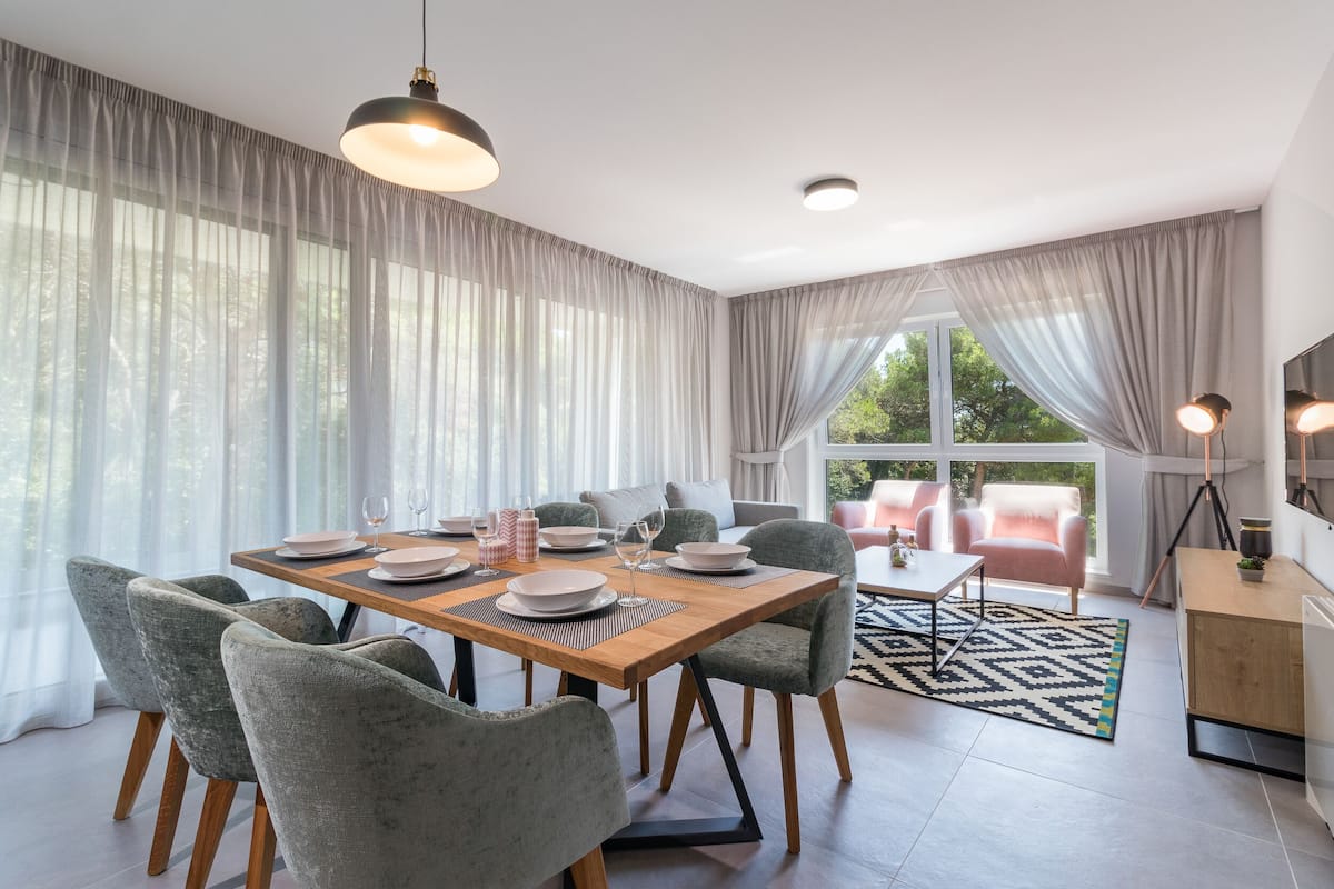 Een moderne eetruimte met een houten tafel, grijs gestoffeerde stoelen en uitzicht op het omliggende landschap door grote ramen.