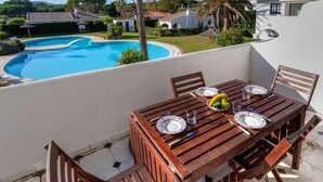 A wooden table set for dining with plates and cutlery, overlooking a swimming pool and a residential area with houses and palm trees. - Nice apartment for 4 guests with WIFI, pool, TV and terrace (Torroella De Montgrí)