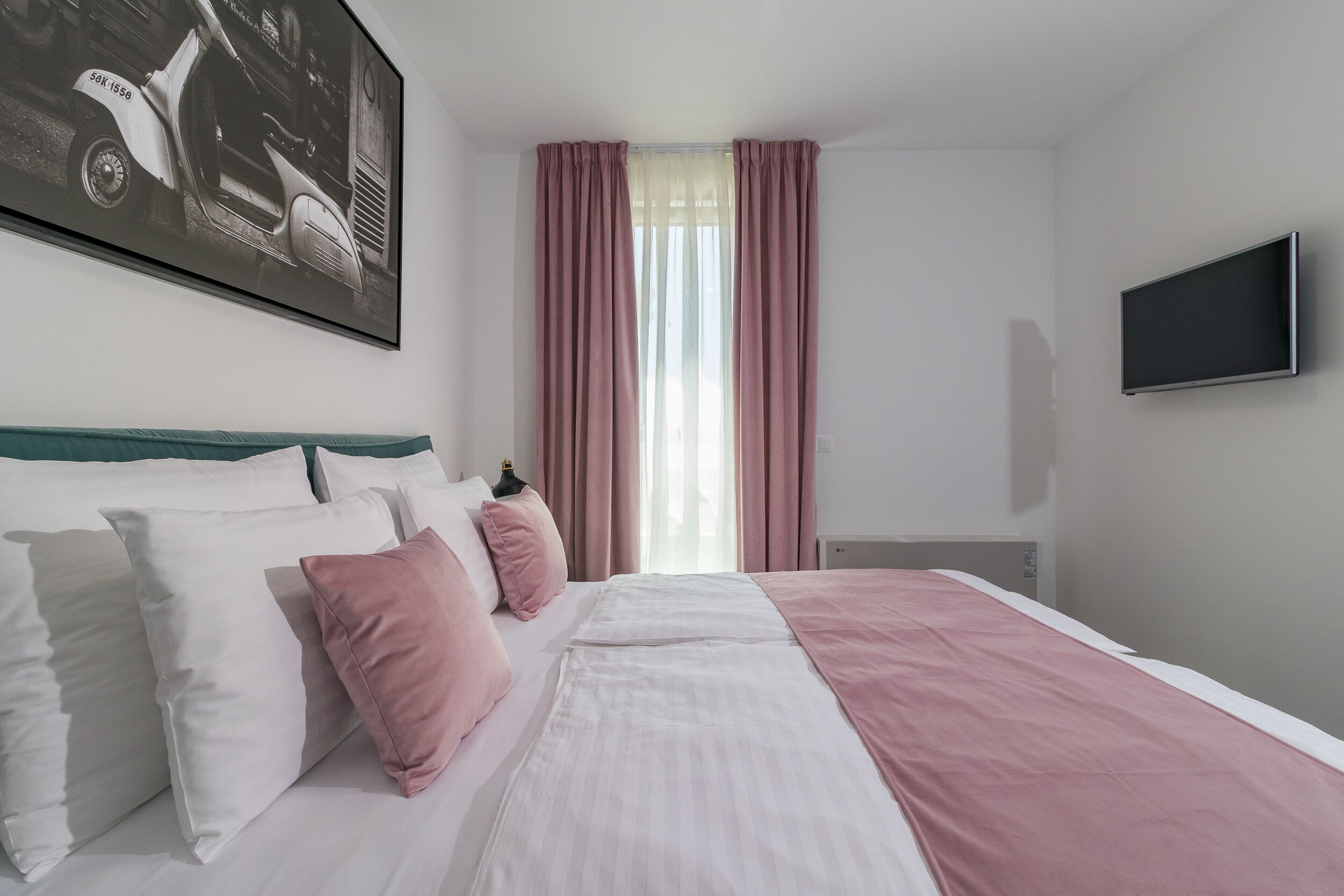 A hotel room with a bed, pillows, a TV, and a window with curtains.