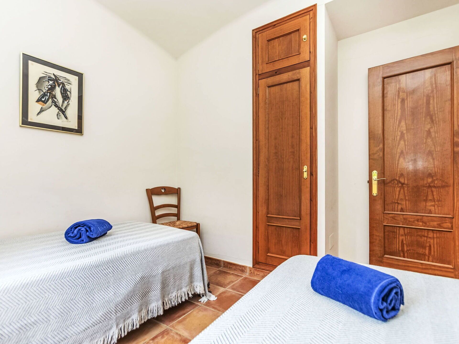 A room with two single beds, a wooden door, a chair, and a framed picture on the wall.