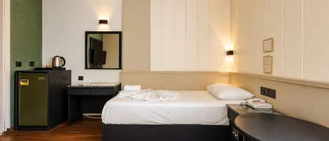 A hotel room with a bed, bedside table, desk, and a small kitchenette.