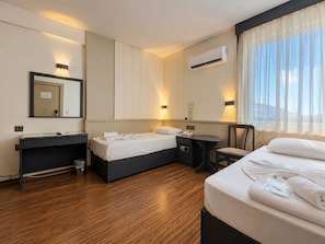 Una habitación de hotel con cama, mesita de noche, silla y escritorio con otra silla.
