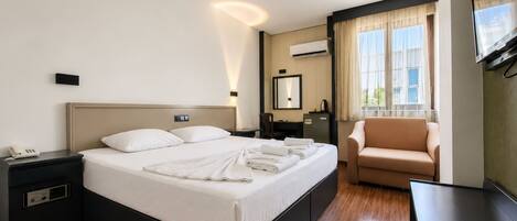 A hotel room with a bed, a chair, a desk, a TV, and a window with curtains.