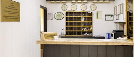 Un comptoir d’accueil avec une pancarte indiquant « RÉCEPTION », une horloge murale, un panneau d’accueil encadré et une étagère contenant divers objets.