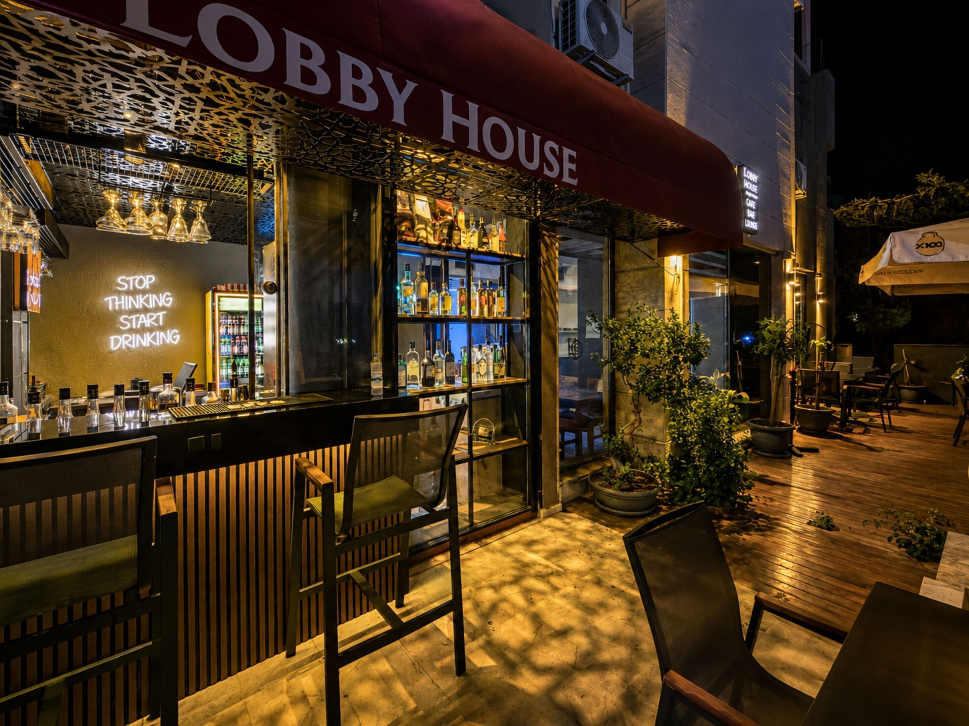 An outdoor bar area with a 'Lobby House' sign, bar counter with stools, and a variety of bottles.