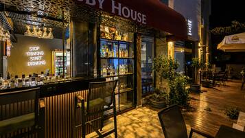 An outdoor bar area with a 'Lobby House' sign, bar counter with stools, and a variety of bottles.