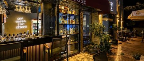 An outdoor bar area with a 'Lobby House' sign, bar counter with stools, and a variety of bottles.