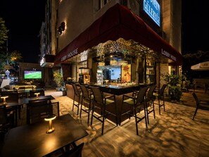 Zona de bar al aire libre con asientos y una pantalla de televisión.