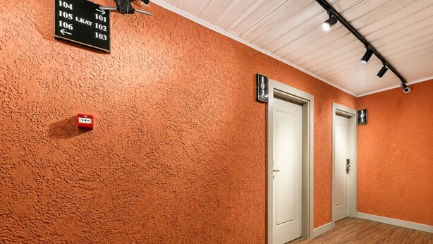 Un pasillo con paredes naranja texturizadas, piso de madera y puertas con los números 101, 102 y 103.